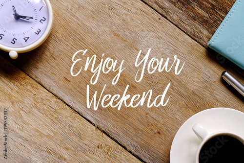 Fotografía Top view of a cup of coffee,clock,notebook and pen on wooden background written with ENJOY YOUR WEEKEND