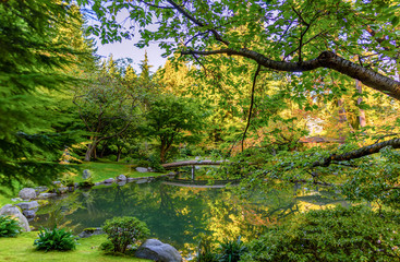 Lake with an ornate wooden bridge, trees and a veranda roof in a park