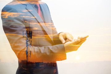Wall Mural - double exposure of businessman using smart phone with silhouette of mobile communication antennas in an orange suns 