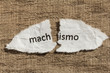 Torn paper written machismo, portuguese and spanish word for chauvism, over wood table. Concept of old and abandoned idea or practice.