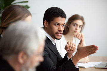 Serious african american ceo giving instructions at diverse team meeting, confident black leader talking delegating work, serious dark-skinned executive manager speaking appealing to colleagues group