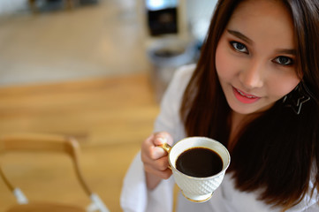 beautiful woman holding a cup of coffee in her hand in blur background coffee shop, vintage style