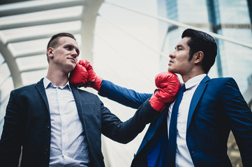 Caucasian businessman wear black suit and Asian businessman man wear blue suit with red boxing gloves fighting by punch and uppercut. concept of business competition.