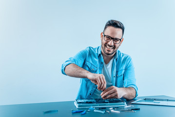 Smiling young technician with eyeglasses working on laptop hardware.