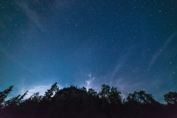 milky way and starry sky with wispy clouds along a steep cliff at night