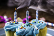 three yellow cupcakes with blue icing sprinkles and candles on blue plate right after candles were blown out