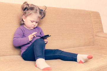 little girl playing smartphone sitting on sofa