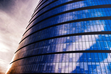 a glass skyscraper with reflection of the sun and clouds above it at dawn.