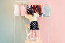 Soft Focus Of A Two Years Old Child Choosing Her Own Dresses From Kids Cloth Rack
