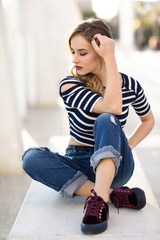 Wall Mural - Blonde woman, model of fashion, sitting in urban background.