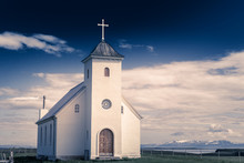 Flateyjarkirkja White Lutheran Church With Meadow In Foreground And Sea  Fjord With Dark Blue Sky And Mountains In The Background, Flatey, Iceland