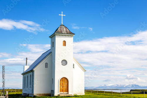 Fotografía Flateyjarkirkja white lutheran church with meadow in foreground and sea fjord w
