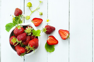 fresh ripe and under ripe strawberry fruits, flowers, leaves on white wood table background