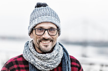 Portrait Of Urban Man In Winter Knitted Wear. Portrait Of Man In Glasses And Knitted White-blue Scarf And Hat. Portrait Of Happy Man. Smiled Non Shaved Guy On Outdoor Background