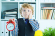 Disappointed kid boss holding a big red alarm clock in his hand suggesting you are late for work.