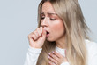 Unhealthy young blonde woman coughing a lot, suffering with cough, has a chest pain, has flu symptom, isolated on gray background. Cold, sickness, bronchitis concept