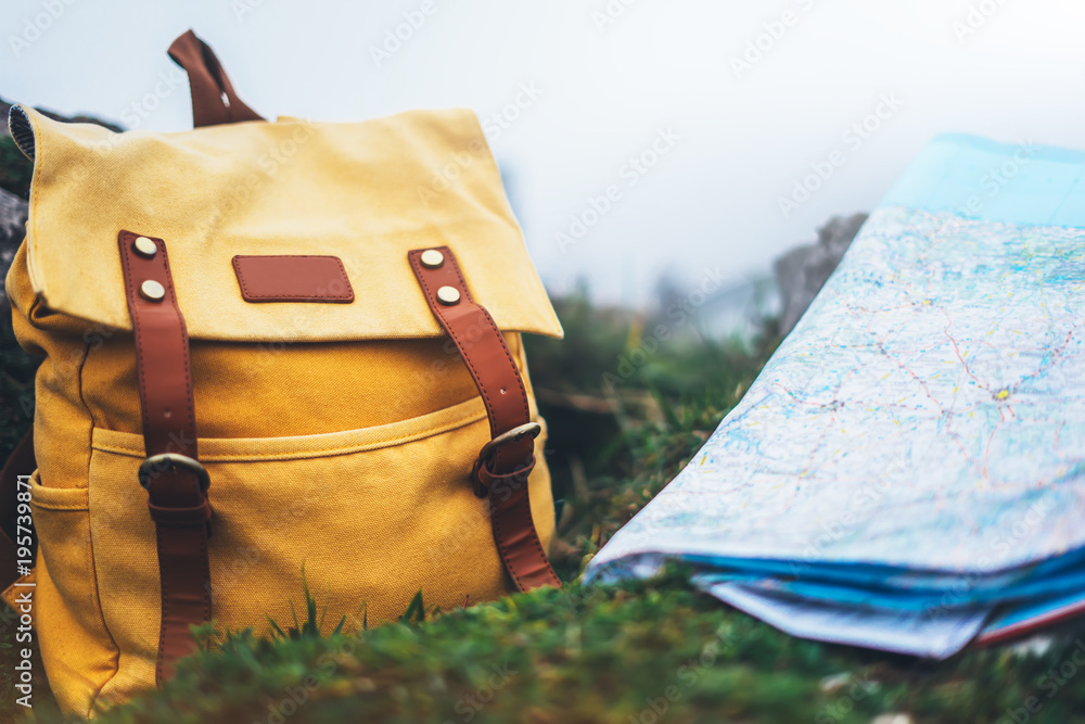 Hipster hiker tourist yellow backpack and navigation map europe on background green grass nature, blurred panoramic landscape, traveler holiday concept, view planning way road in trip vacation - obrazy, fototapety, plakaty 