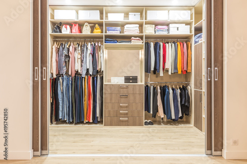 Modern Wooden Wardrobe With Clothes Hanging On Rail In Walk In