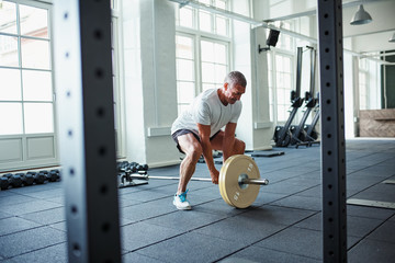 Wall Mural - Senior man in sportswear lifting weights alone in a gym