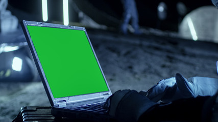 Wall Mural - astronaut on the alien planet works on a mock-up green screen laptop. in the background her crew mem