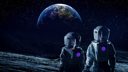 Wall Mural - two astronauts in space suits standing on the moon and look at beautiful earth in the sky. space tra