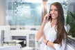 © Bojan - Portrait of cheerful young lady talking on phone in office.