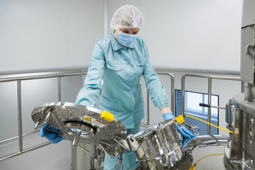 Wall Mural - Pharmaceutical factory woman worker in protective clothing operating production line in sterile environment