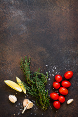 Wall Mural - Ingredients for cooking on a dark stone table - thyme, cherry tomato, garlic and lemon. Copy space, top view flat lay background.