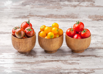 Wall Mural - Colorful tomatoes in three wooden jars on white wooden background