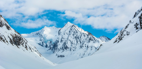 Wall Mural - Alpine landscape with peaks covered by snow and clouds