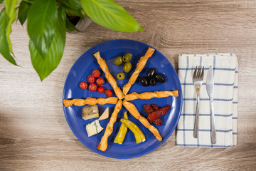 top view mediterranean antipasti plate with two kinds of olives tomatoes cheese filled peppers separated by breadsticks