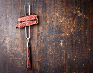 Slices of beef steak on meat fork on dark wooden background