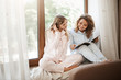 © Cookie Studio - Indoor shot of relaxed happy caucasian sisters sitting at home on window sill in cute nightwear, reading articles in magazine, discussing latest trend in fashion industry or picking new clothes