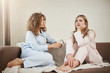© Cookie Studio - Who need psychologist when you have best friend. Two women sitting on sofa in nightwear in cozy room, discussing personal problems, focused and bothered with issue. Girl tries to comfort girlfriend