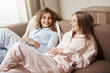 © Cookie Studio - Friendship is before relationship. Beautiful european girls lying on sofa in cozy nightwear, talking and having fun, discussing life and watching movie on TV, spending leisure at home