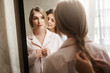 © Cookie Studio - Close-up portrait of two beautiful women at home. Attractive young blonde standing near mirror, changing clothes from pyjamas and waiting while mother combing braid. Typical cozy morning in family