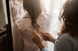 © Cookie Studio - Cropped shot of mother and daughter standing in nightwear while mom making braid for her cutie, combing hair and looking in mirror to see result, getting dressed in morning