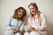 © Cookie Studio - Let me show you funny video. Portrait of beautiful caucasian blond sister in nightwear spending leisure with friend, holding digital tablet while reading hilarious joke or article, having fun together