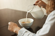 © Cookie Studio - Cereals is best breakfast to keep fit. Cropped shot of woman sitting in nightwear pouring milk in bowl with cereals, preparing meal to eat and ran to work, listening news on TV