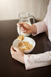 © Cookie Studio - Vertical cropped shot of woman sitting in kitchen holding spoon while eating bowl of cereals with milk, having healthy breakfast and enjoying beautiful morning with family, discussing plans for today