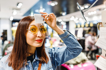 Wall Mural - Happy eastern woman buying and choosing stylish sunglasses in shop in the Mall