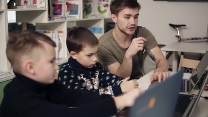 attarctive male programmer teacher with several tattooes on his arms explaining something to his two
