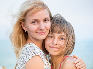 mother hugging her daughter at sea, outdoor. happy loving family. woman and girl with embracing look