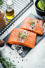 Two pieces of raw salmon fillet with fresh herb rosemary, spices and olive oil on black slate plate