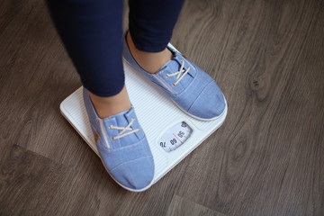 Wall Mural - Overweight girl standing on floor scales indoors