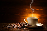 Fototapeta Kawa jest smaczna - Cup of coffee with smoke and coffee beans on old wooden background