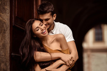 Happy Young Female With Long Dark Hair Glad To Recieve Passionate Kiss From Her Boyfriend. Handsome Male Embraces His Girlfriend And Kisses. Portrait Of Lovely Young Couple Express Mutual Love.