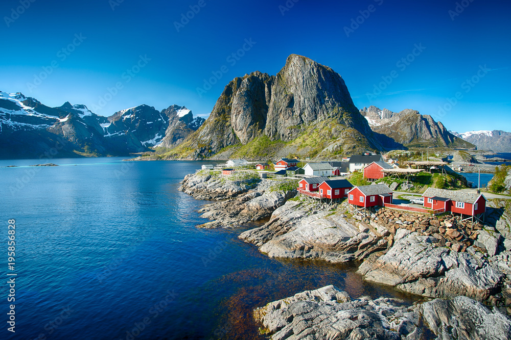 The village of Reine under a sunny, blue sky, with the typical red rorbu houses. - obrazy, fototapety, plakaty 