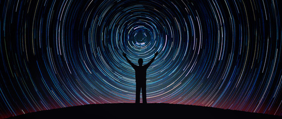 Wall Mural - Man silhouette on a night sky background with bright stars trails. Man watching the stars. Science, education and religion team concept background. Elements of this image furnished by NASA. 