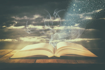 image of open antique book over wooden table with flying pages.